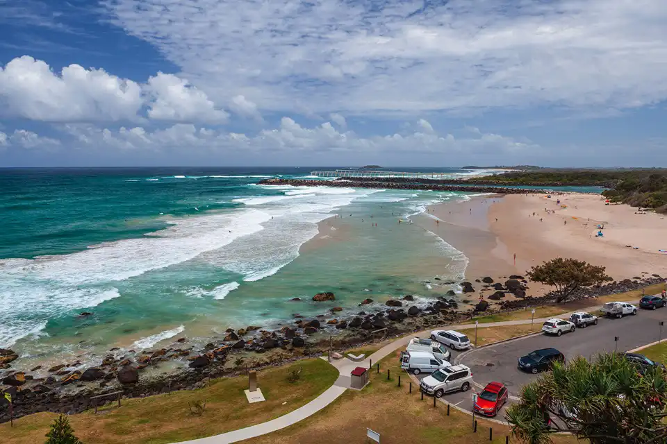 Scenic coastal beach with turquoise waves and car park.