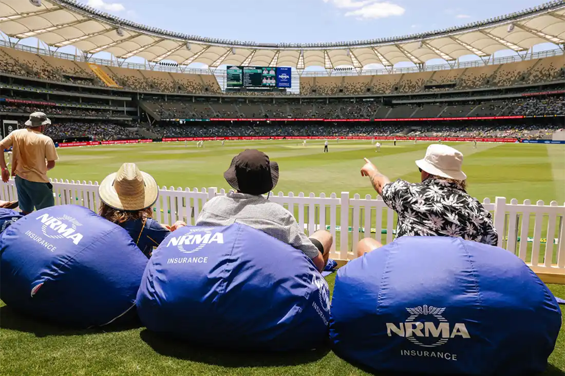 3 people with hats, sitting on NRMA Insurance bean bags, in the sun watching the cricket.