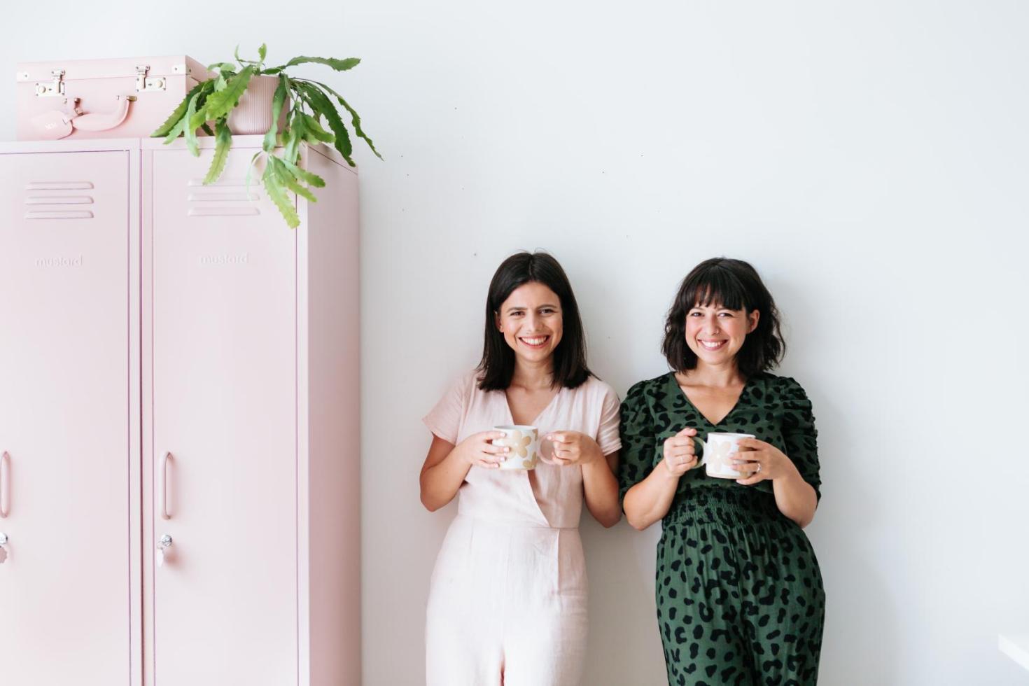 Becca and Jess leaning against wall with cup of tea