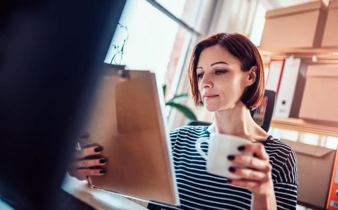 Person holding a coffee cup and looking at clipboard