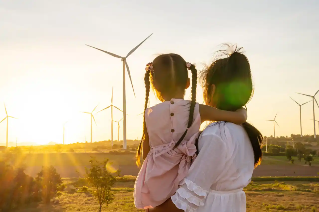 Parent holding a child looking out to wind turbines in the distance