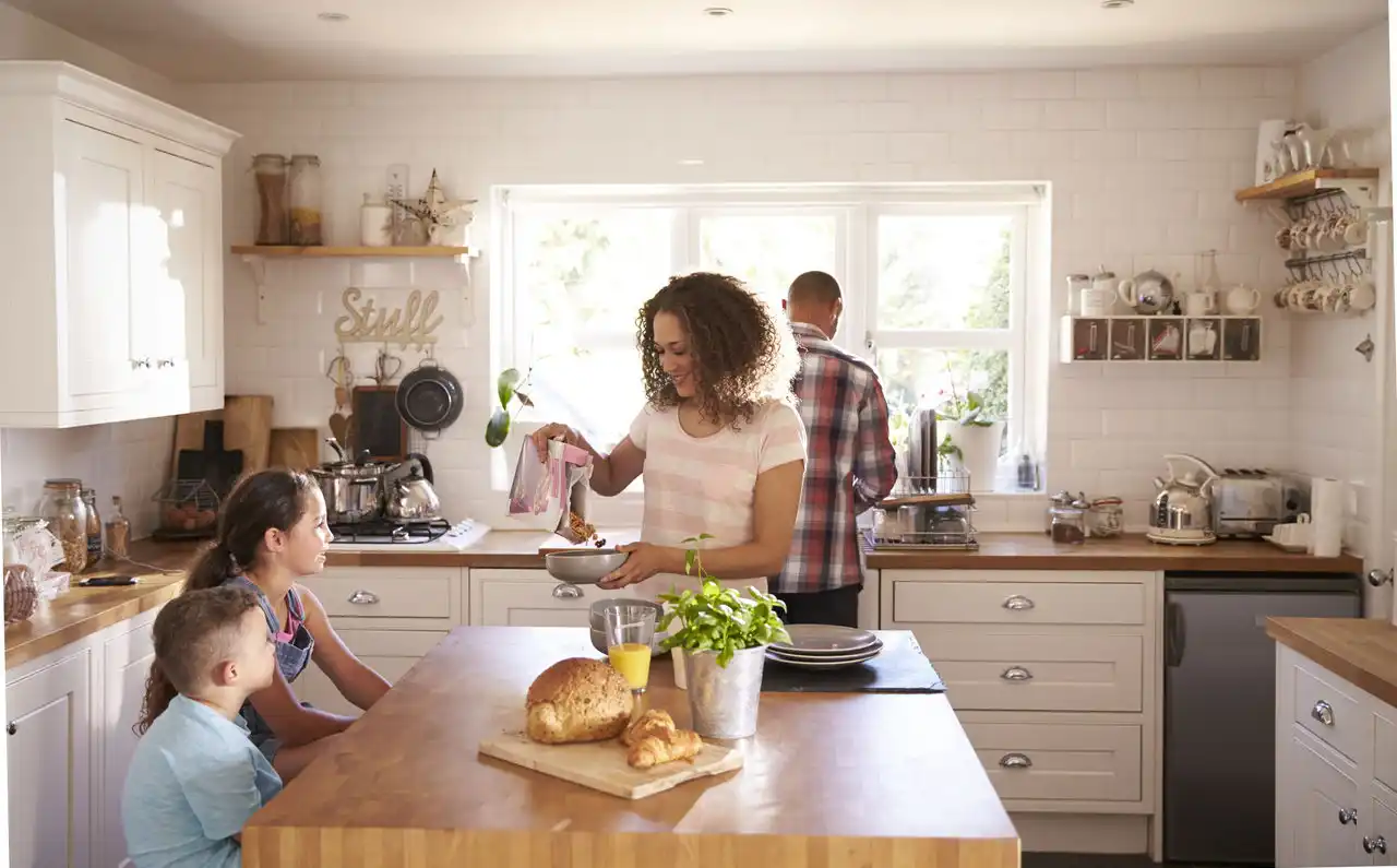 Parent pouring cereal, other parent at sink, children at table