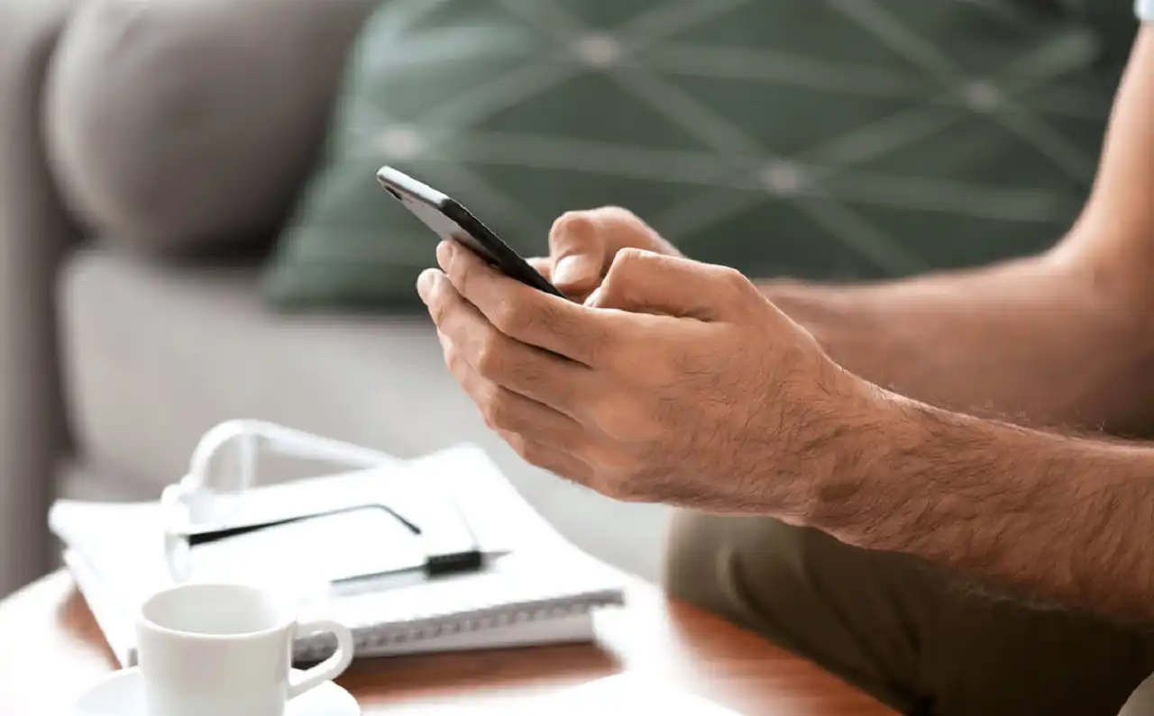 Close up of phone in both hands typing and glasses resting on coffee table