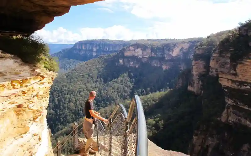 Person standing on a walk way facing away from camera and admiring Blue Mountains NSW