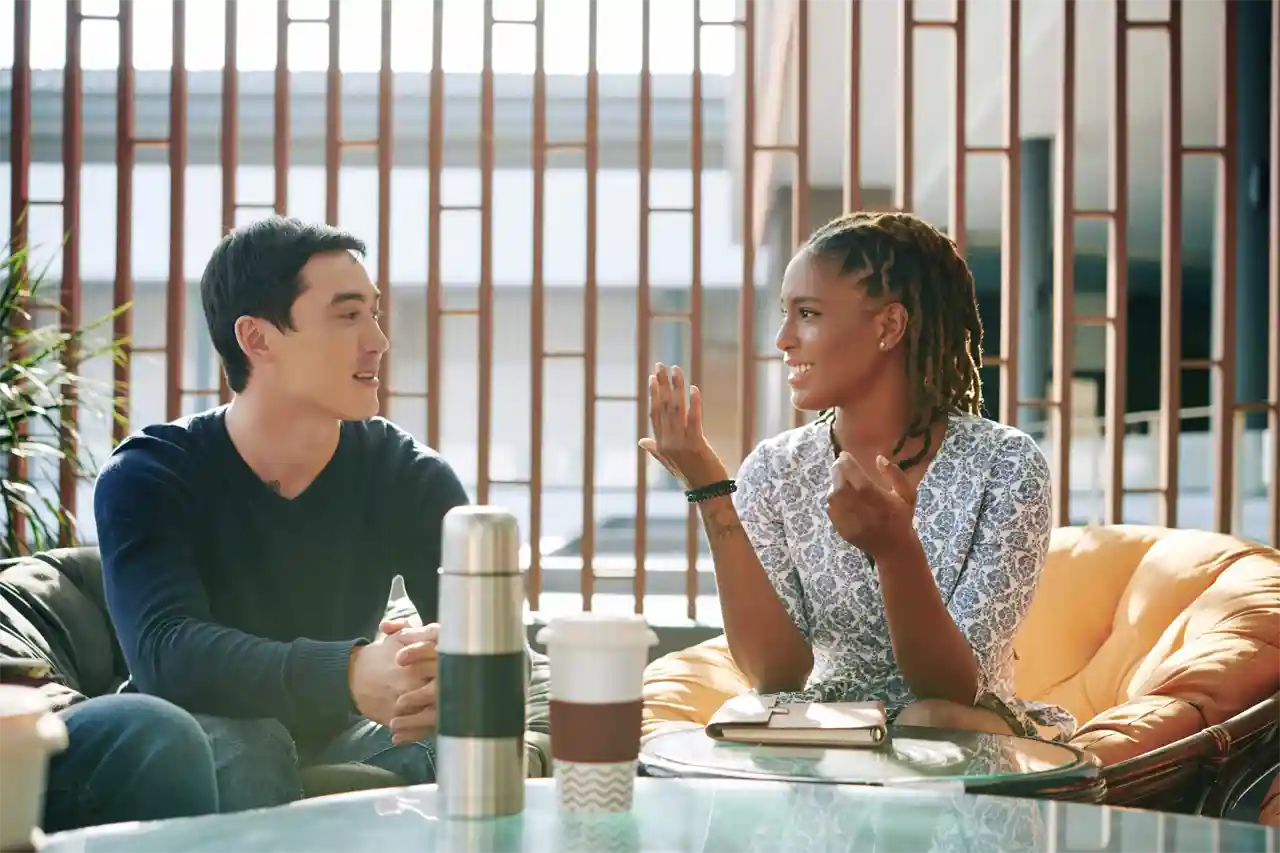 Two people sitting at a table, with a coffee cup and thermos in the foreground