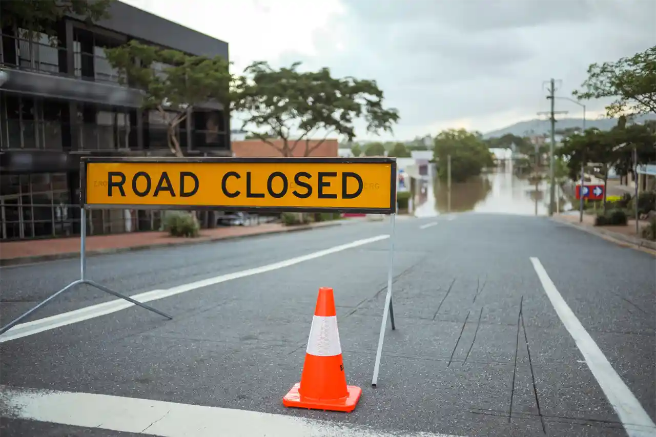 Road closed sign and witches hat showing flooded street behind