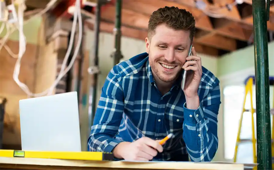 Person in a checked shirt, leaning on a bench at a construction site on the phone