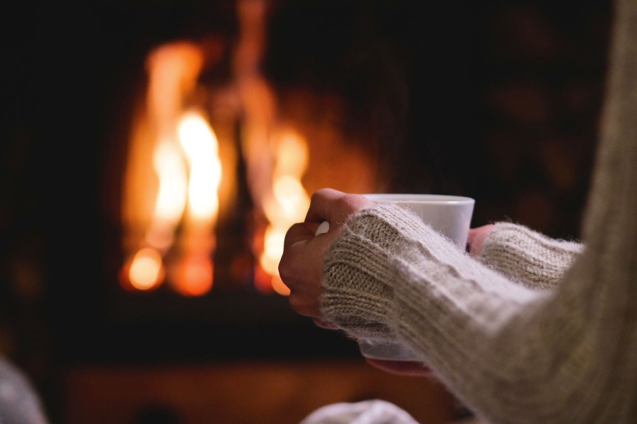 Person sits in front of fireplace holding a mug.
