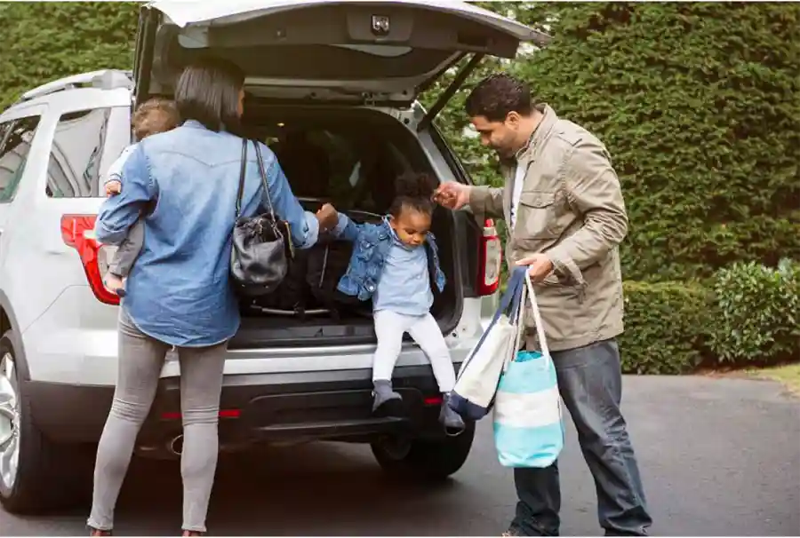 Parents helping child jump down from the back of the car 