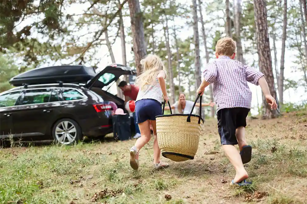 Kids running towards parent with straw bag as other parent packs car