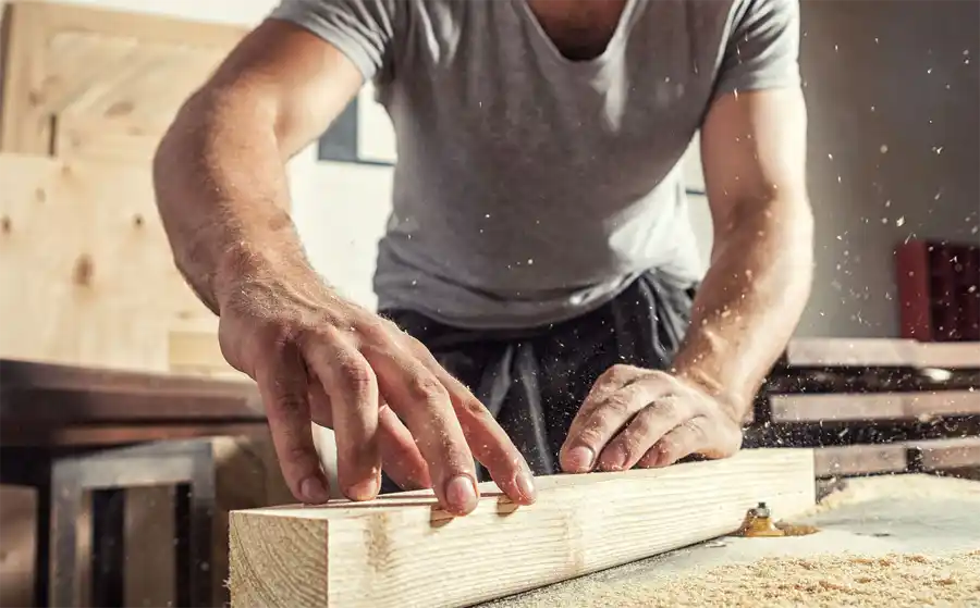 Close up of a person holding a piece of timer and using an electric tool