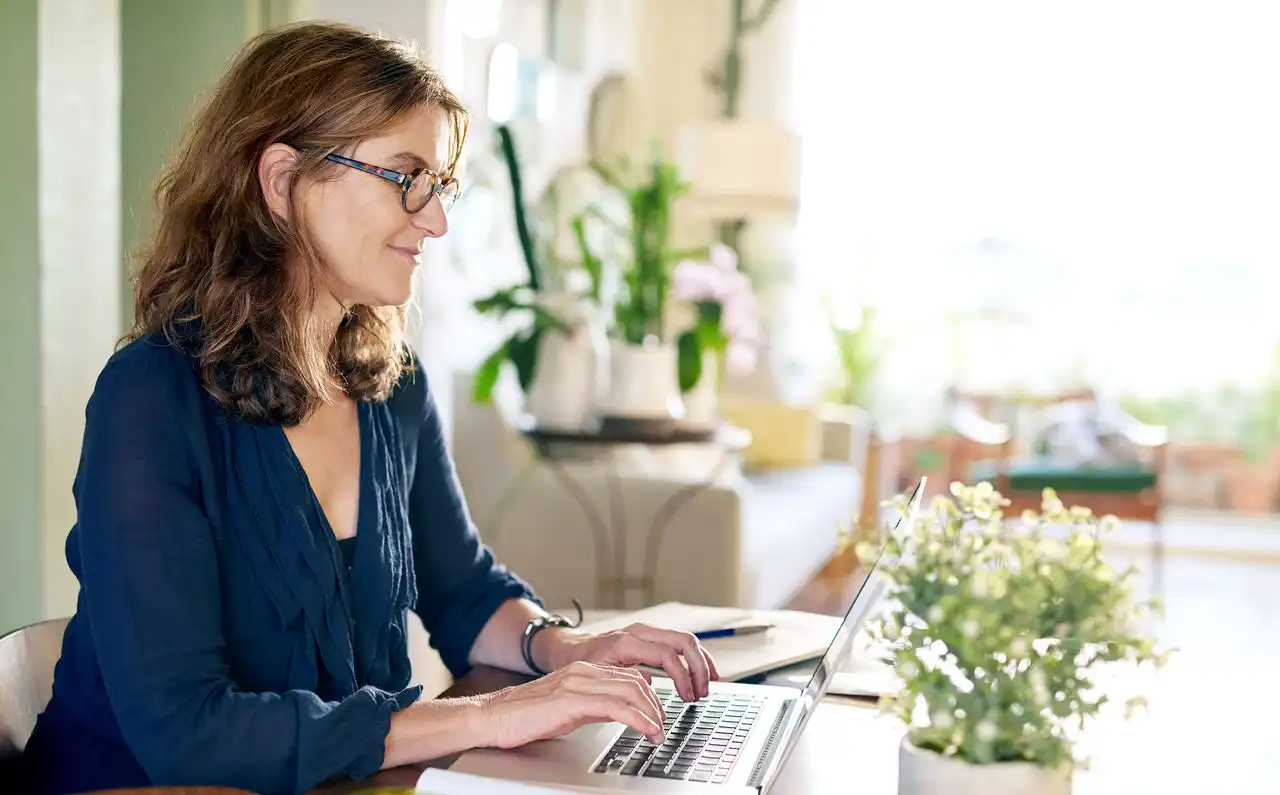 Person on laptop in a shared lounge and dining room with flowers