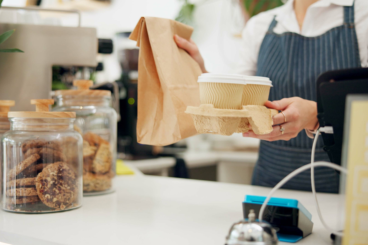 Barista hands take-away coffees and treats over a counter